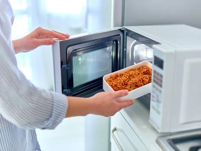 Person placing white casserole dish of cooked rice into a microwave oven
