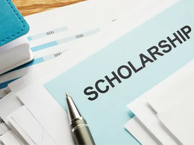 Envelope labeled SCHOLARSHIP on documents with pen and stacked papers