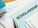 Envelope labeled SCHOLARSHIP on documents with pen and stacked papers