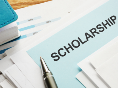 Envelope labeled SCHOLARSHIP on documents with pen and stacked papers
