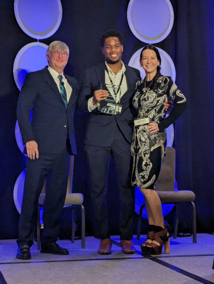 Man holding award between man and woman in front of conference background