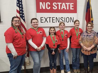 Six people wearing red shirts and medals standing under sign reading "NC STATE EXTENSION"