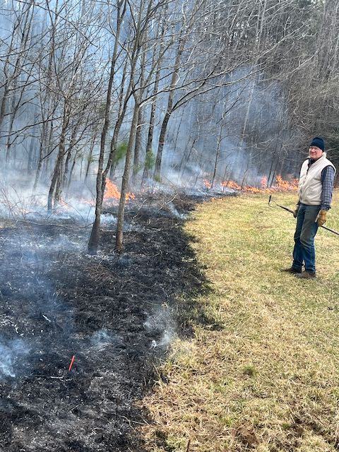 A man stands beside burning brush.