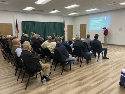 Man pointing at projected slide while audience sits in rows in a meeting room