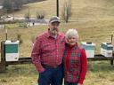 Older couple standing next to wooden beehives on a grassy hillside