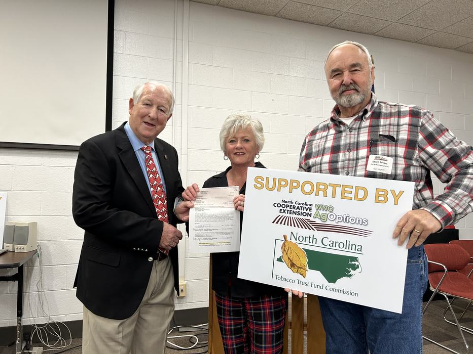 Three people holding a sign reading "SUPPORTED BY" and "North Carolina Tobacco Trust Fund Commission."