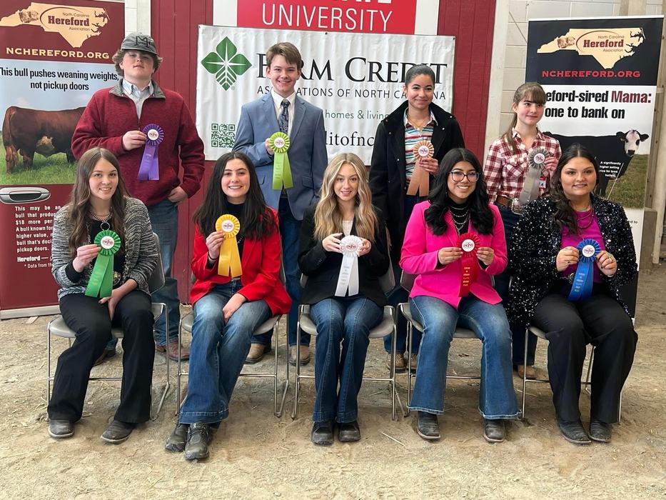 Nine youth holding award ribbons at a livestock show, "UNIVERSITY" banner behind