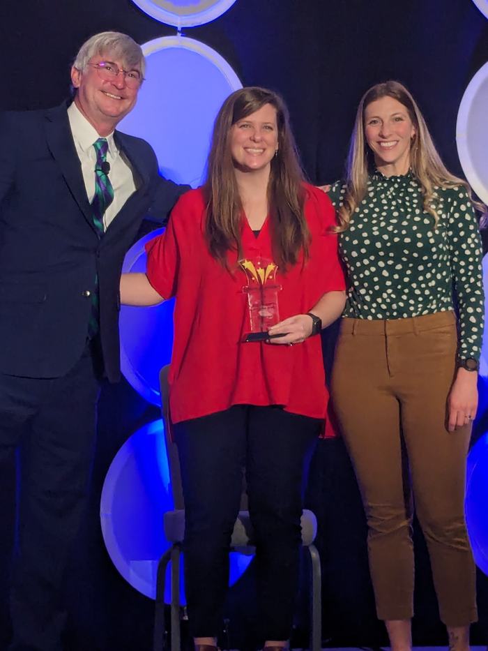 Woman winning award posing on stage with award between man and woman presenting the award.