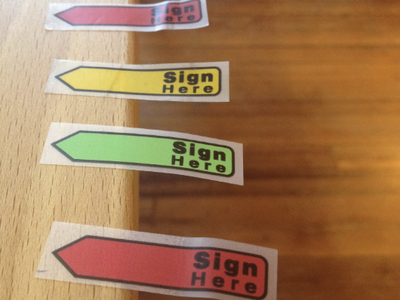 Colored arrow stickers reading "Sign Here" lined along wooden table edge