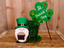 Gnome holding a glitter pot beside a green shamrock sign reading "St. Patrick's Day"
