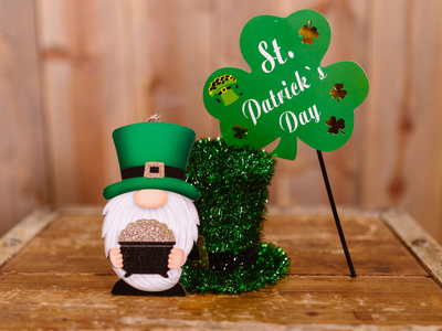 Gnome holding a glitter pot beside a green shamrock sign reading "St. Patrick's Day"