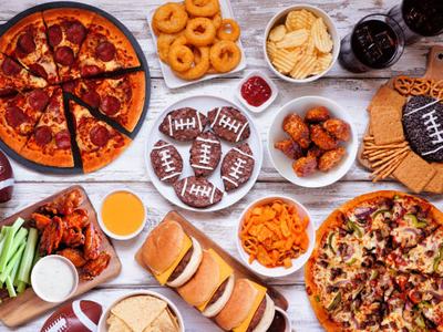 Super Bowl or football theme food table scene. Pizza, hamburgers, wings, snacks and sides. Above view on a white wood background.