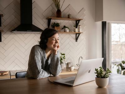 Person wearing headphones smiling while using a laptop at a kitchen table
