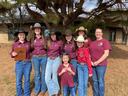 Group of eight girls and women in maroon shirts and cowboy hats standing outdoors
