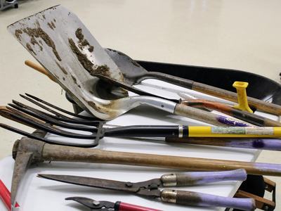 Muddy shovels, pitchfork, shears and handles laid on a table with a black wheelbarrow