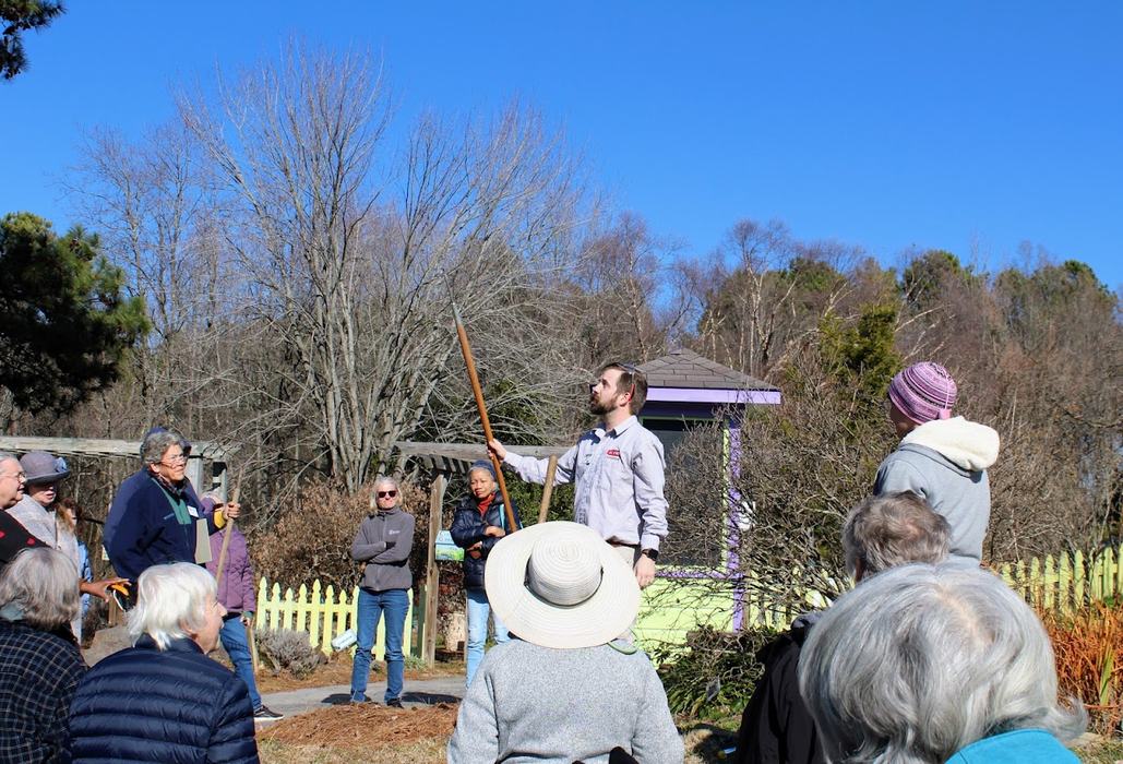A man holds a tool in front of a group of people to demonstrate its use.