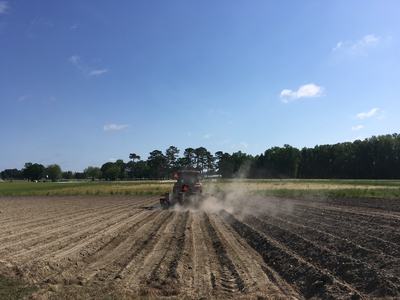 Tractor tilling a plowed field with dust rising behind it