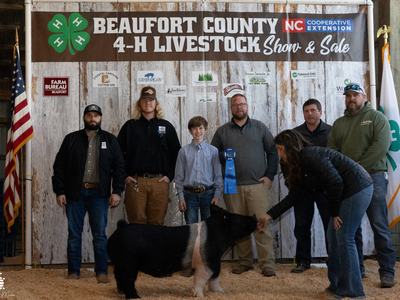 Picture of Dylan Briley with his hog and the buyers of his animal in front of the 4-H Livestock Show banner.