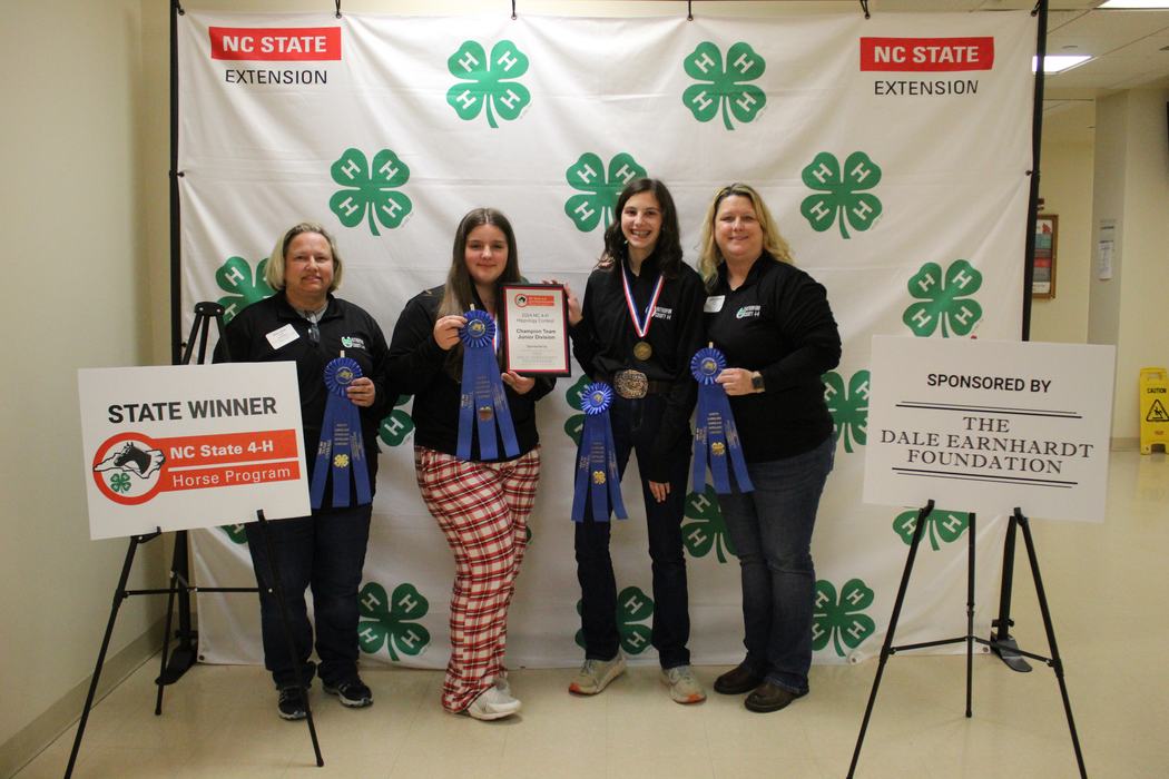 Four people with blue ribbons and plaque before 4‑H backdrop; signs read "STATE WINNER" and "THE DALE EARNHARDT FOUNDATION"