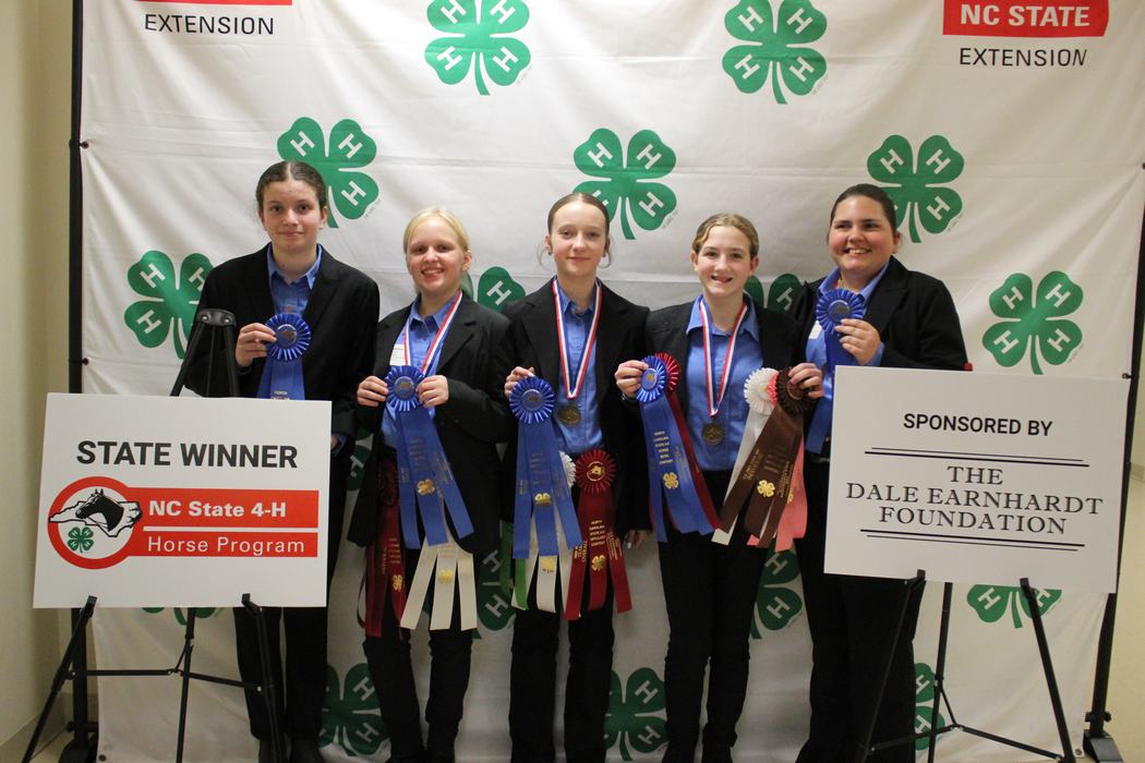 Five 4-H youths holding ribbons and medals; signs read "STATE WINNER NC State 4‑H Horse Program" and "Dale Earnhardt Foundation"