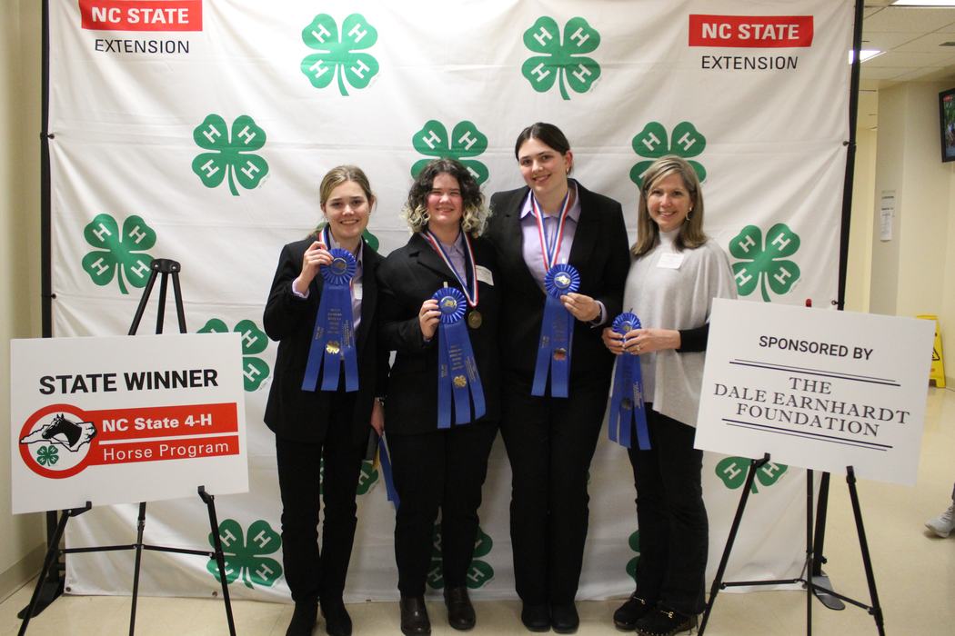 Four award winners holding blue ribbons before "NC STATE EXTENSION" backdrop and "STATE WINNER" sign