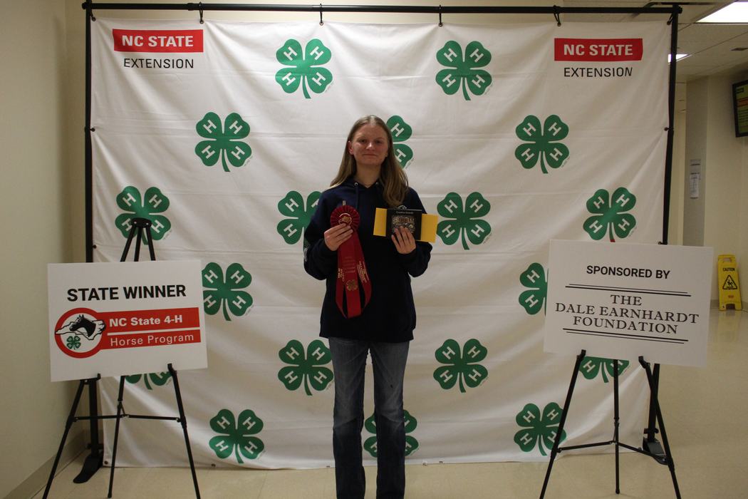 Teen holding red ribbon and award in front of NC State Extension 4‑H backdrop