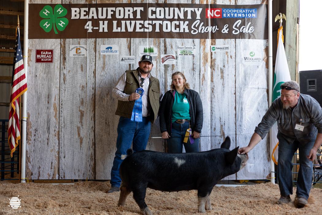A kid posing with a ribbon and a pig.