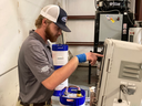 Worker pointing at industrial control panel beside blue chemical containers