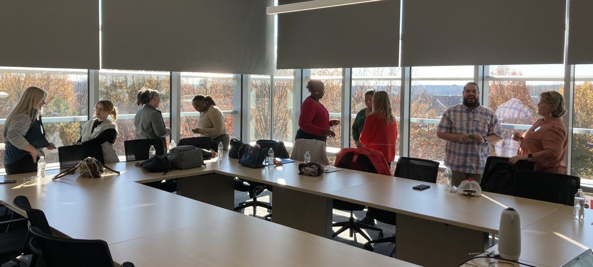 A group of people stand around a conference table having side conversations.