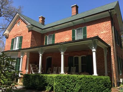 Two-story red brick house with green shutters and a covered porch with rocking chairs
