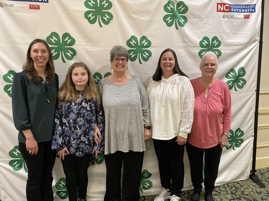Five women pose together in front of a 4-H Banner