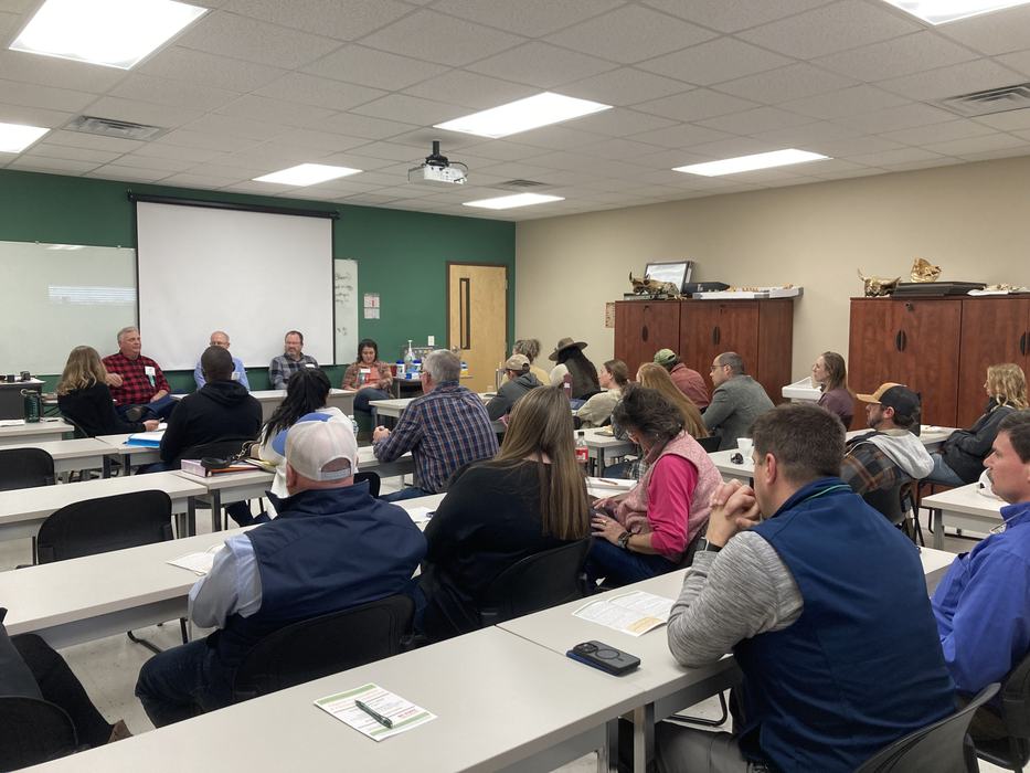 A group of people in a room listening to a panel of speakers.