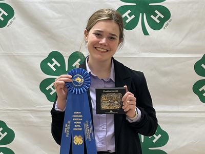 Person holding blue ribbon reading "North Carolina State 4-H Horse Bowl Contest" and a plaque