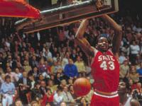 Basketball player in red "STATE 43" jersey dunking ball during game with crowd
