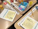 Hands at classroom desks with skeleton worksheets, pencils, Play‑Doh, scissors, water bottle