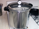 Large stainless-steel pressure canner with lid and dial thermometer on gas stovetop