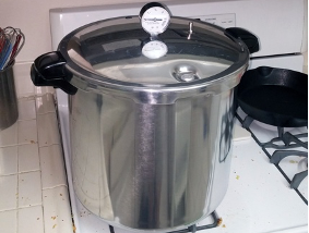 Large stainless-steel pressure canner with lid and dial thermometer on gas stovetop