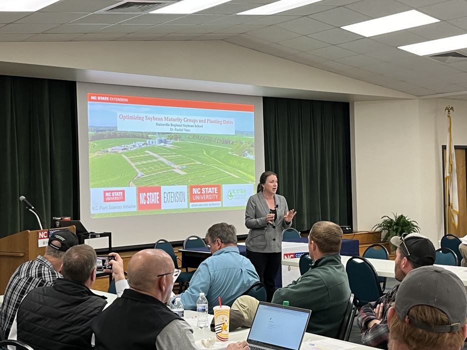 Presenter speaking in front of projected slide "Optimizing Soybean Maturity Groups and Planting Dates"