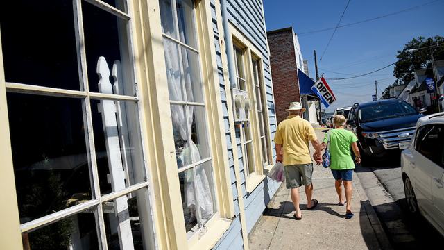 A couple walks on the sidewalk next to buildings downtown. 