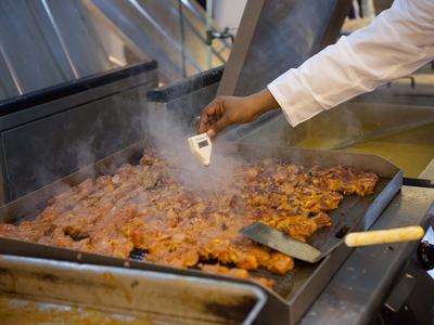 Person checking internal temperature of food being cooked on griddle.