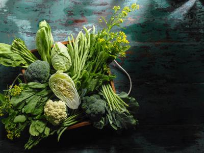 Market fresh green leaf vegetables in an old wooden crate on an old wooden turquoise table. Vegetables include, broccoli, cauliflower, cabbage, spring greens, bok choy, spinach and choy sum.