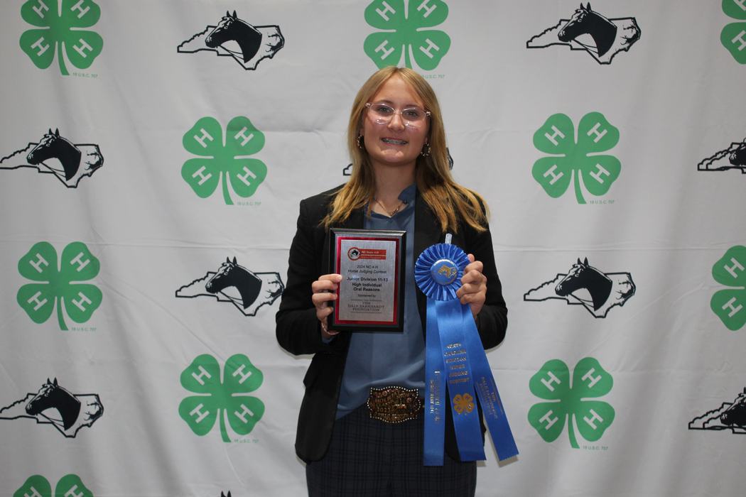 Young person holding plaque reading "High Individual" and a blue ribbon against 4-H backdrop