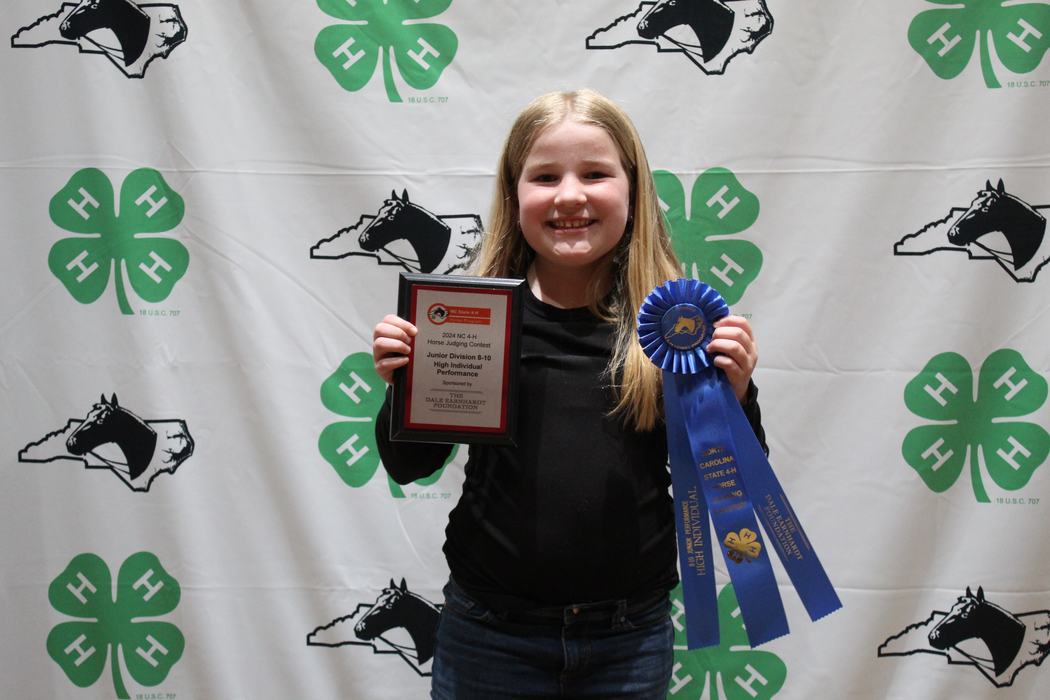 Young person holding plaque reading "2024 NC 4‑H Horse Judging Contest" and a blue ribbon