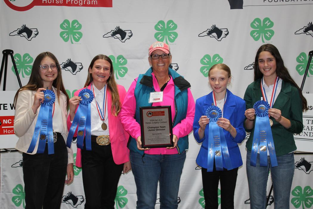 Five people holding blue ribbons and plaque reading 'Champion Team Junior Division' at 4‑H backdrop