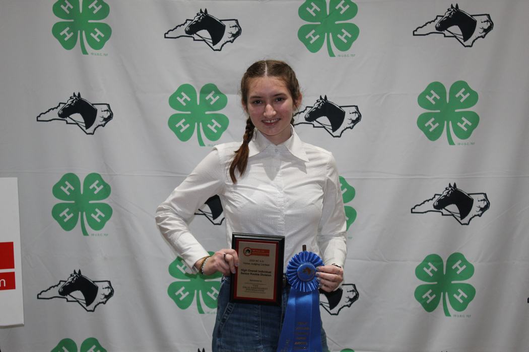 Young woman holding a plaque and blue ribbon in front of 4‑H clover backdrop