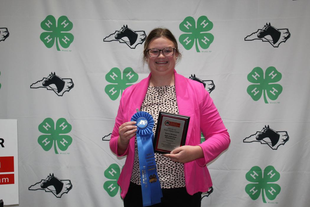 Person holding blue ribbon and plaque in front of 4‑H clover backdrop