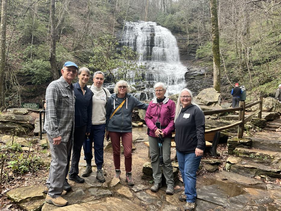 Hikers pose together in front of a waterfall.