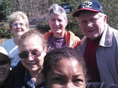 Six adults posing for a close outdoor selfie in a garden-like setting