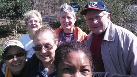 Six adults posing for a close outdoor selfie in a garden-like setting