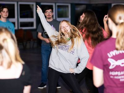 Teen girl dancing with arm raised among a group of people indoors
